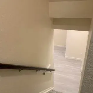 Staircase descending into a hallway with light-colored walls and flooring, a wooden handrail.