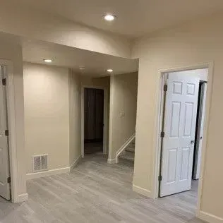Interior view of a hallway and open doorways with light gray flooring and cream-colored walls.