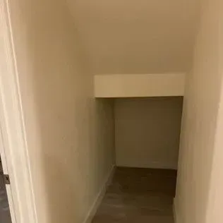 A small, empty closet with beige walls and a dark wooden floor.