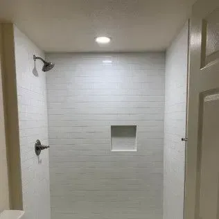 White tiled shower with a niche and showerhead.