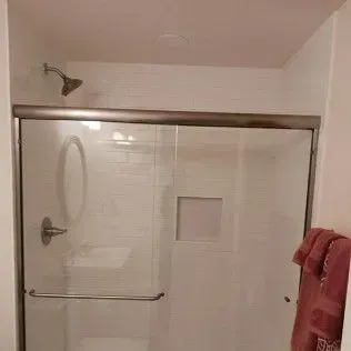 Shower with glass doors and a white tile interior. A showerhead and bar are visible.