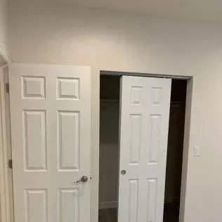 Two white doors, one open leading to a closet with clothes. The closet door is sliding.