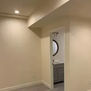 An open doorway leads to a bathroom with a mirror. Room is painted light beige.