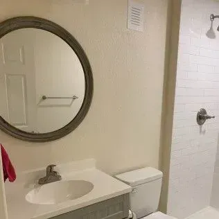 Bathroom with a round mirror, white sink, toilet, and white tile shower.