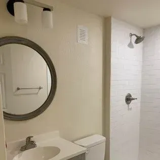 Bathroom with round mirror, sink, toilet, and white tile shower.