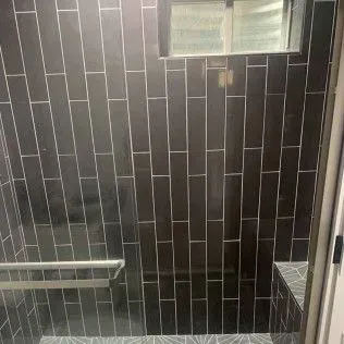 Black tiled shower with window, grab bar, and bench.