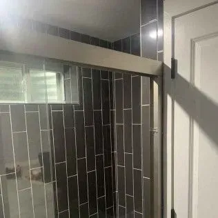 Dark gray tiled shower with a glass door and a white door frame.