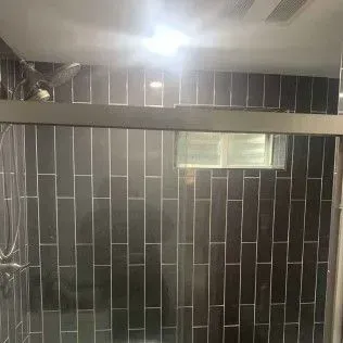 Dark gray tiled shower interior with glass sliding door and overhead light.