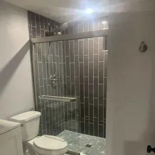 A small bathroom with a glass-enclosed shower, toilet, and gray tiling.