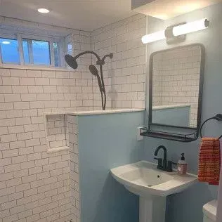 Bathroom with white subway tile shower, blue wall, sink, and mirror.