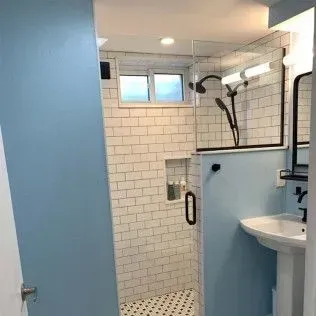 Modern bathroom with blue walls, subway tile shower, and pedestal sink.