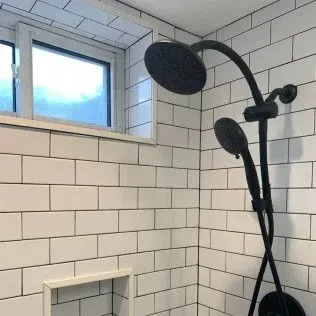 Black shower fixtures on white subway tile in a shower, with a window.