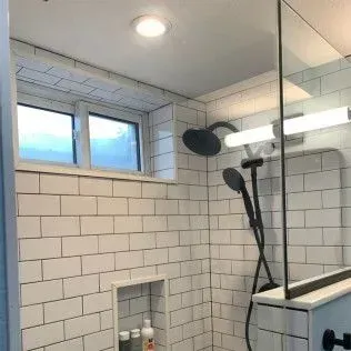 White tiled shower with black fixtures and a window.