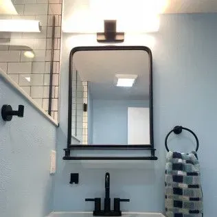Bathroom with black framed mirror, towel ring, faucet, and light fixture; blue walls.