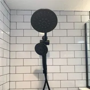 Black showerhead with handheld sprayer against white subway tile in a shower.
