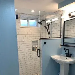 Bathroom with blue walls, white subway tile shower, pedestal sink, and black accents.