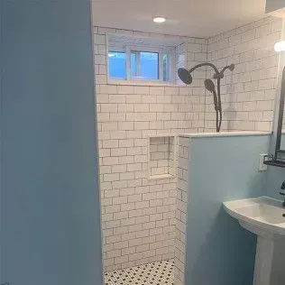 Bathroom with subway tile shower, blue walls, pedestal sink, and window.