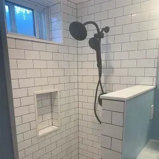 White tiled shower with a dark shower head, a recessed shelf, and a small window.