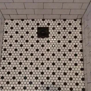 Shower floor with black and white hexagonal tiles and central drain.