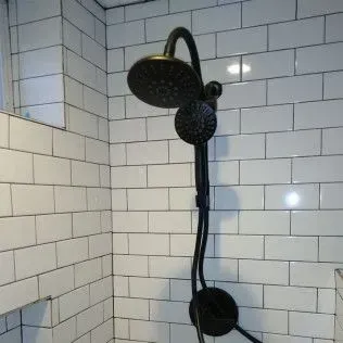 Black shower head and handheld shower against white tiled wall.