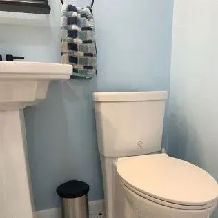 A bathroom with a toilet, sink, wastebasket, and towel hanging. Light blue walls.