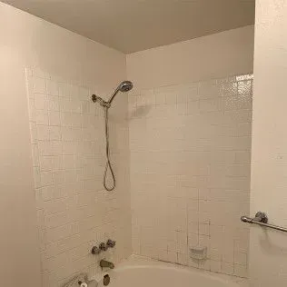 White tiled shower with handheld showerhead and faucet fixtures.