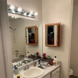 Bathroom with mirror, medicine cabinet, and cluttered sink countertop. Light-colored walls.