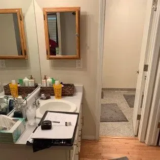 Bathroom interior: vanity, mirror, medicine cabinet, open doorway to room with rugs.