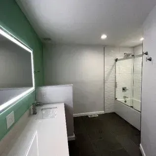 Modern bathroom with a bathtub, glass shower doors, and a large mirror with a lighted frame.