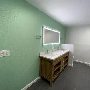 Bathroom with green wall, wooden vanity, lit mirror, and dark tile floor.