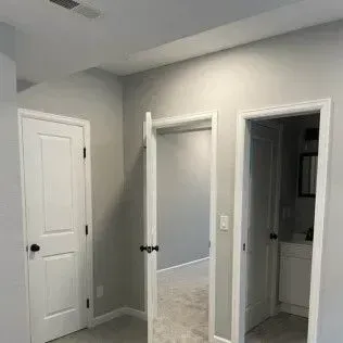 Three white interior doors in a hallway, two closed and one open, painted gray walls.