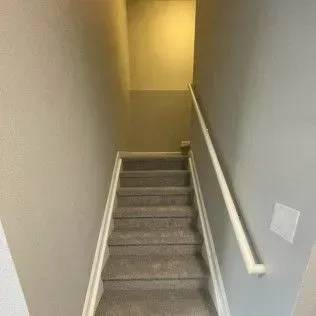 Staircase with gray carpet, white handrail, and light gray walls.