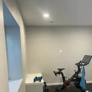 Exercise bike in a gray-walled room, with dumbbells on a white shelf. A towel hangs from the bike.