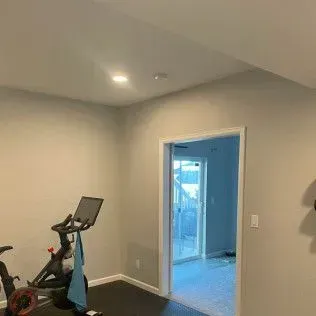 Stationary bike in a room with a doorway leading outside. Neutral-colored walls and ceiling, dark floor.