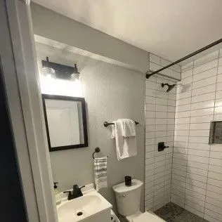 Small bathroom with white subway tile shower, toilet, and sink; black fixtures.