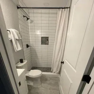 Small bathroom with white tiled shower, toilet, and white door.