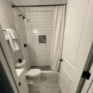 Small bathroom with white subway tile shower, toilet, and white door.