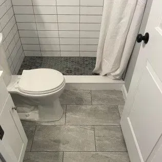 Bathroom with white subway tile shower, toilet, gray floor tile, white door.