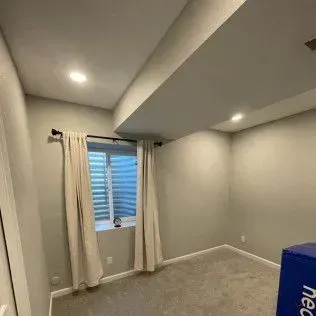 Empty room with a window, curtains, and recessed lighting. Gray walls and carpet.