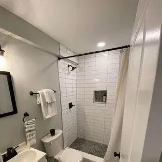 Bathroom with white tiled shower, black fixtures, and gray walls.