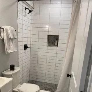 Small bathroom with white tiled shower, black fixtures, and toilet.