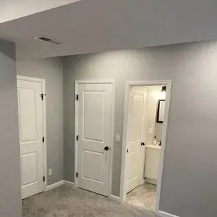 Three white doors in a room, two closed, one open to a bathroom with a sink and mirror.