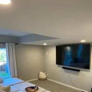 Living room with a large TV mounted on a gray wall, a soundbar, and a sectional couch.