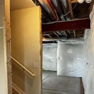 Stairwell doorway leading to a basement. Walls and insulation visible. Handrail along stairs.