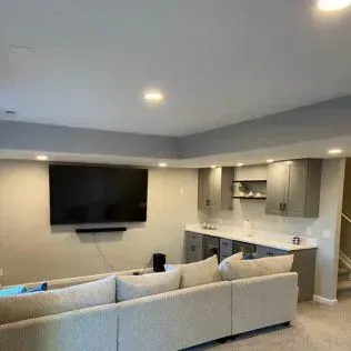 Living room with a large TV, sectional sofa, and a built-in bar area with gray cabinets.