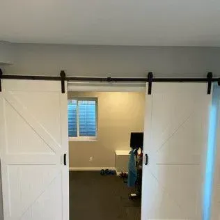 White barn doors on a black track open to a room with a window and black floor.