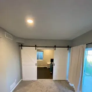 White barn doors on a black track open to a room with a window and a desk.
