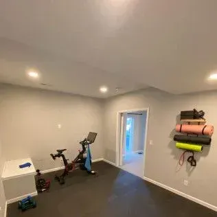 Home gym with exercise bike, yoga mats, weights, and door to outside.