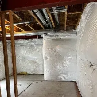 Basement walls insulated with white plastic sheeting, studs and pipes visible.