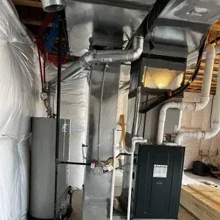 HVAC and water heater in a basement. Ductwork, pipes, and insulation are visible.
